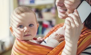 Young mother talking on a phone having her baby in a carrier