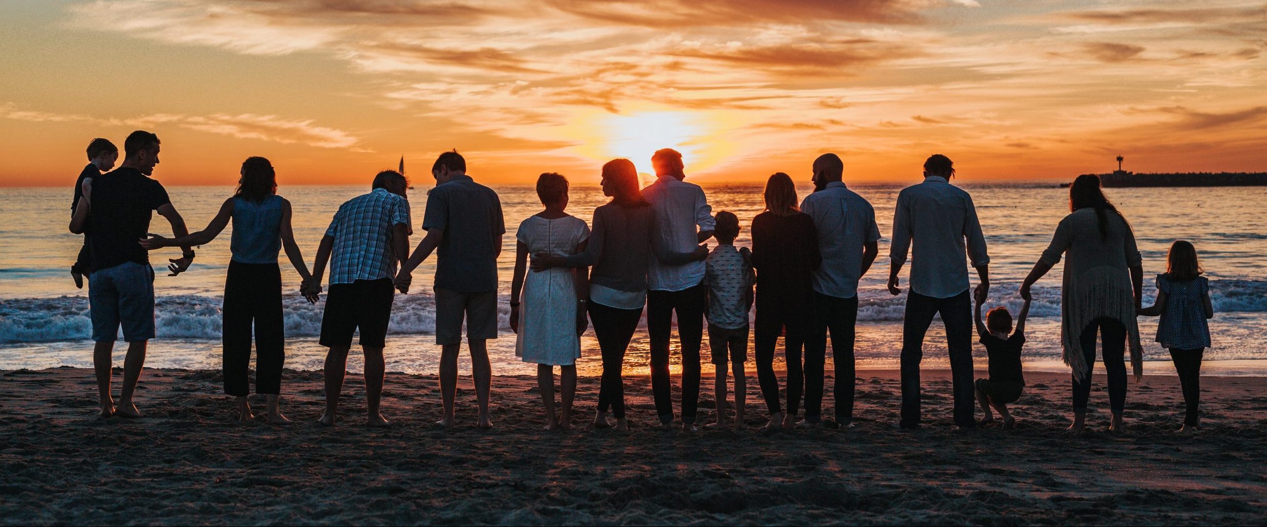 silhouette of family on a beach facing the water against a sunset